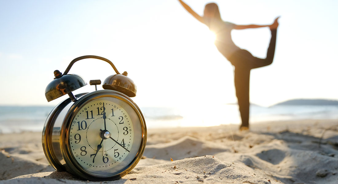 Alarm clock on a beach with a person doing yoga in the background
