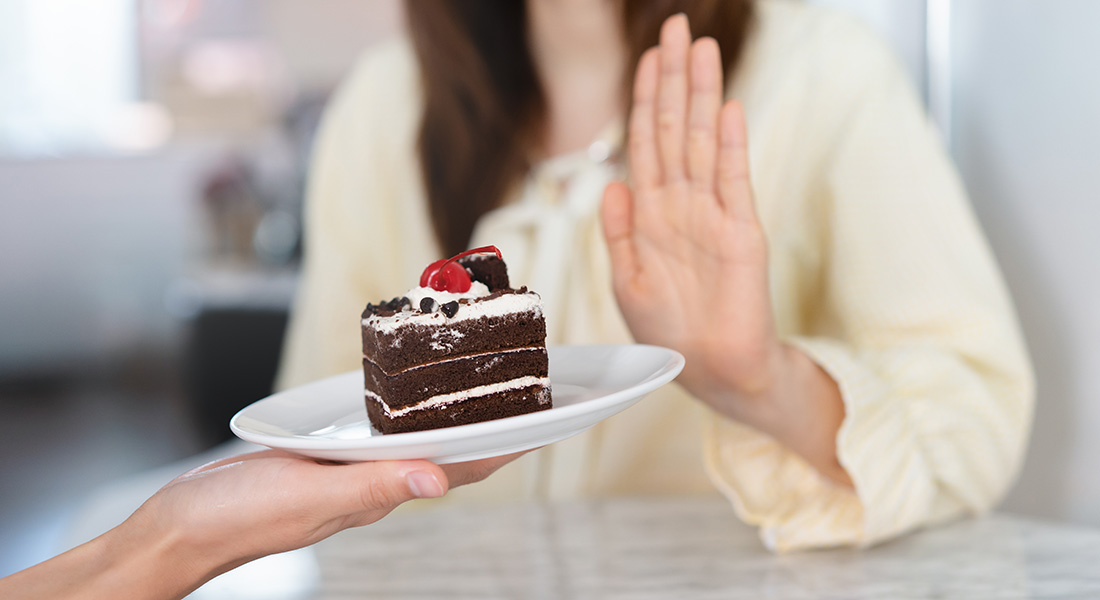 A woman holds her hand up to say to a piece of cake.