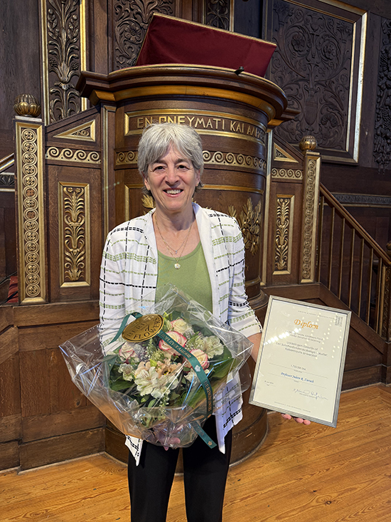 Photo of Juleen holding a bouquet of flowers and the prize certificate